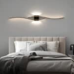 Applique murale ondulée noire en aluminium au-dessus d'un lit moderne avec une tête de lit rembourrée.