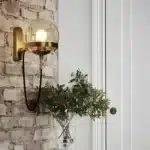 Applique murale nordique moderne en verre avec support doré, installée sur un mur en brique.