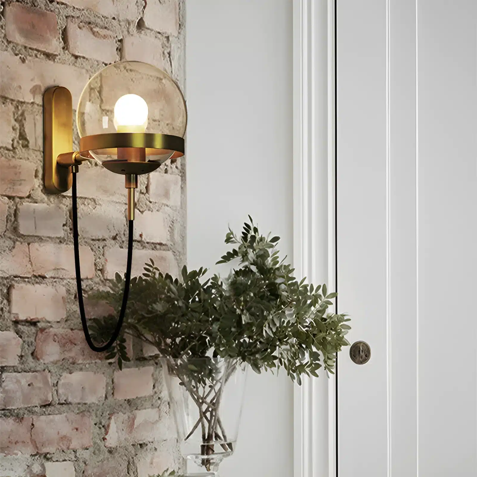 Applique murale nordique moderne en verre avec support doré, installée sur un mur en brique.