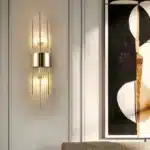 Applique murale moderne en cristal et acier doré, design faisceau, allumée sur mur beige.