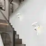 Appliques murales LED en forme de tourbillon blanc, installées le long d'un escalier dans une maison moderne.