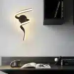 Applique murale LED en forme de tourbillon noir, éclairant un bureau moderne.