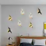 Appliques murales en forme d'oiseaux de couleur blanche, noire et dorée, installées sur un mur blanc.