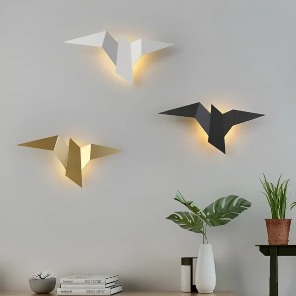 Trois appliques murales en forme d'oiseaux, de couleur blanche, noire et dorée, illuminent un mur.