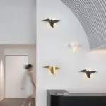Ensemble d'appliques murales en forme d'oiseaux blanches, noires et dorées sur un mur moderne.