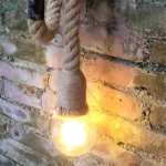 Applique murale en corde de chanvre pour chambre, installée sur un mur de briques, avec ampoule allumée.
