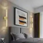 Deux appliques murales LED dorées installées de part et d'autre d'un lit moderne.