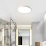 Plafonnier LED minimaliste blanc installé dans une salle de bain moderne.