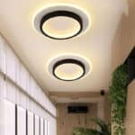 Deux plafonniers LED noirs ronds éclairant un couloir moderne avec des plantes